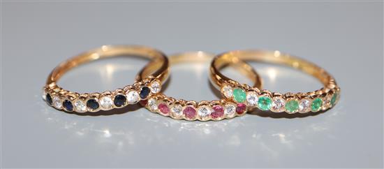 A modern suite of three yellow metal and gem set rings, including emerald, ruby and sapphire, size N/O.